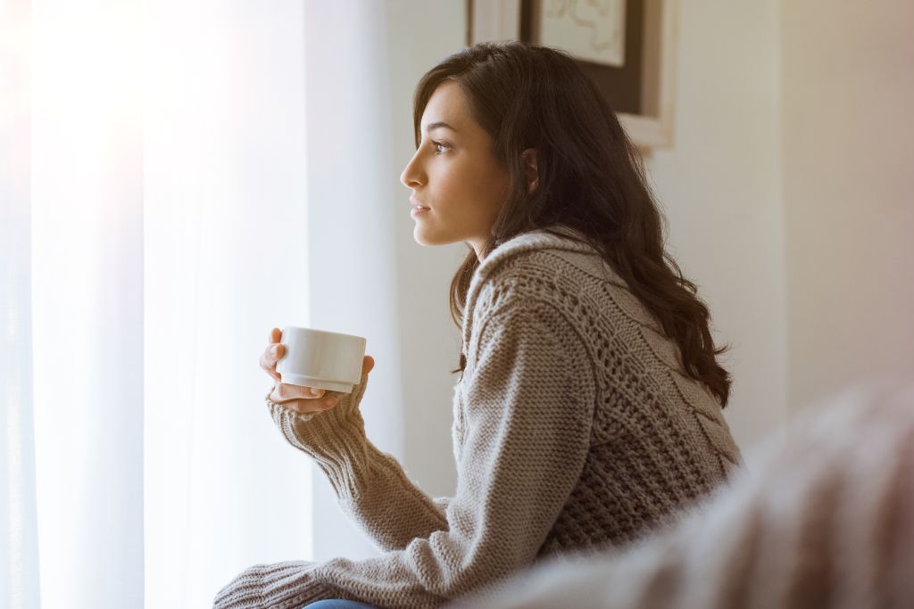 Woman sitting quietly with a cup of tea, reflecting near a window