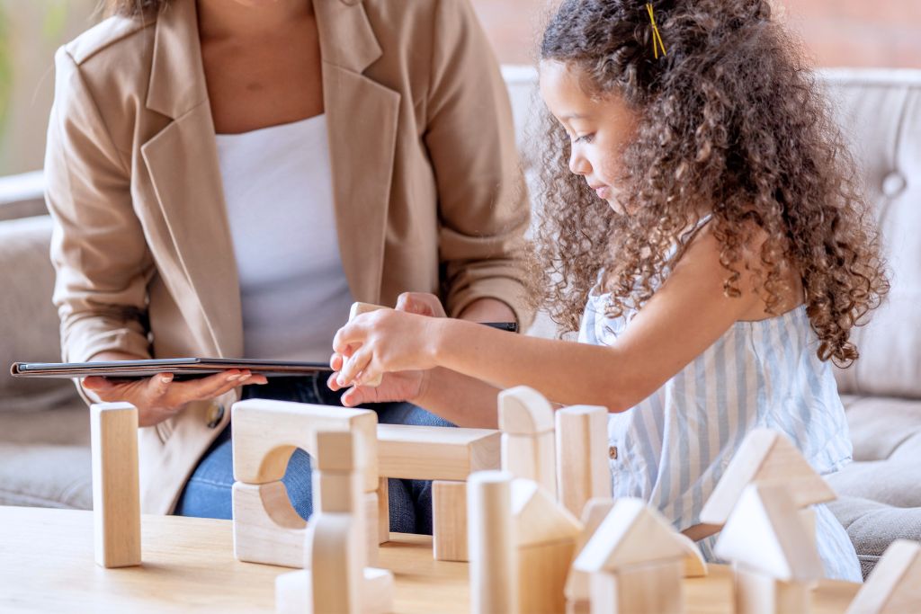 Young girl in therapy playing with wooden blocks during a session with a psychologist