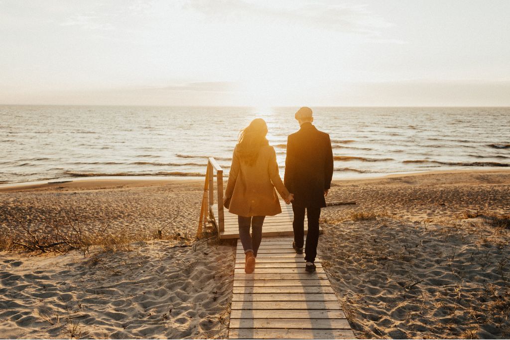 Couple walking side by side along a beach boardwalk at sunset