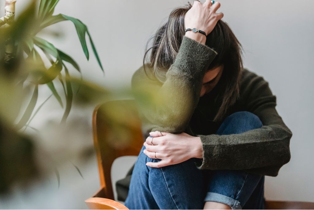 Woman sitting curled up in a chair with her head down, reflecting common signs of depression