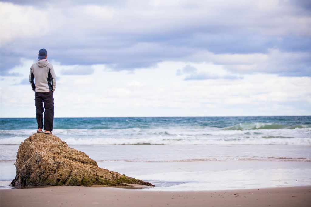 Person standing on a rock facing the ocean, symbolising clarity, calm, and a path forward through support and reflection.