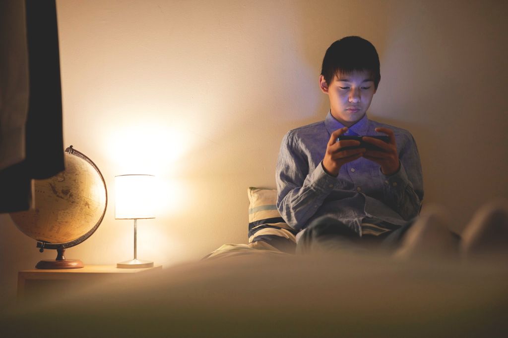 Person sitting alone in a dark room illuminated by their phone screen, reflecting the isolation and compulsive nature of addiction.