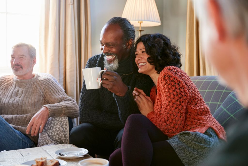 Smiling couple sharing a laugh over tea, representing connection and wellbeing in a healthy relationship