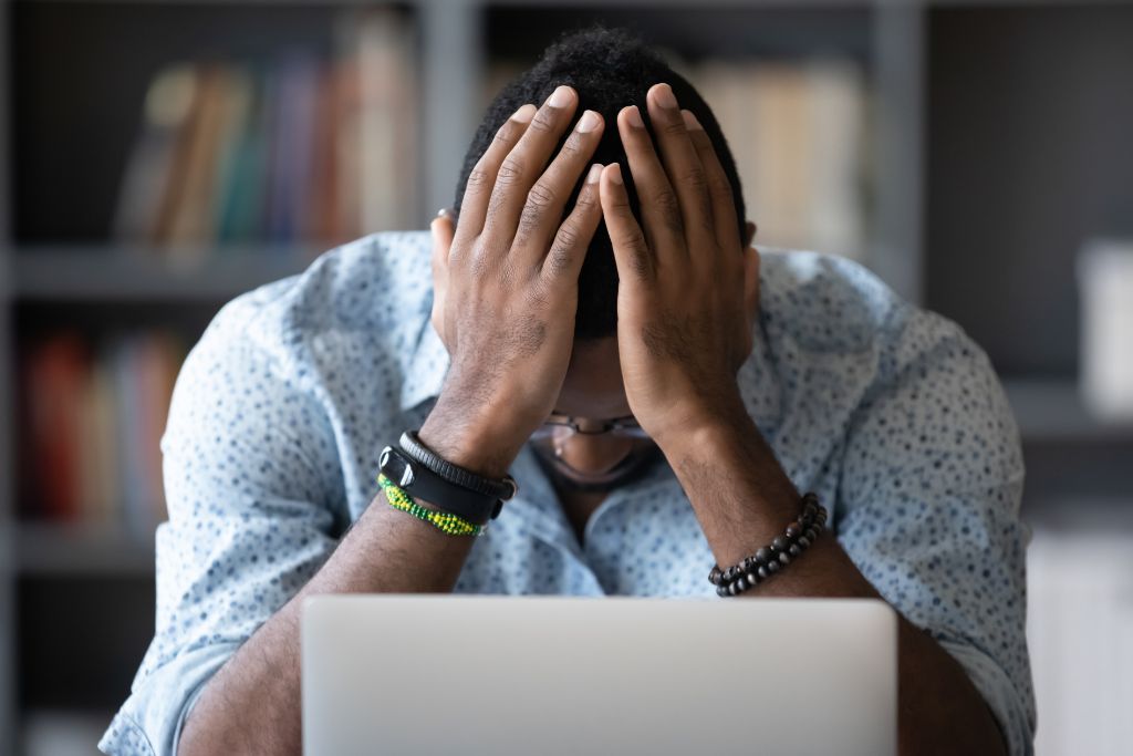 A man sitting with his head in his hands in front of a laptop, showing signs of stress and mental fatigue