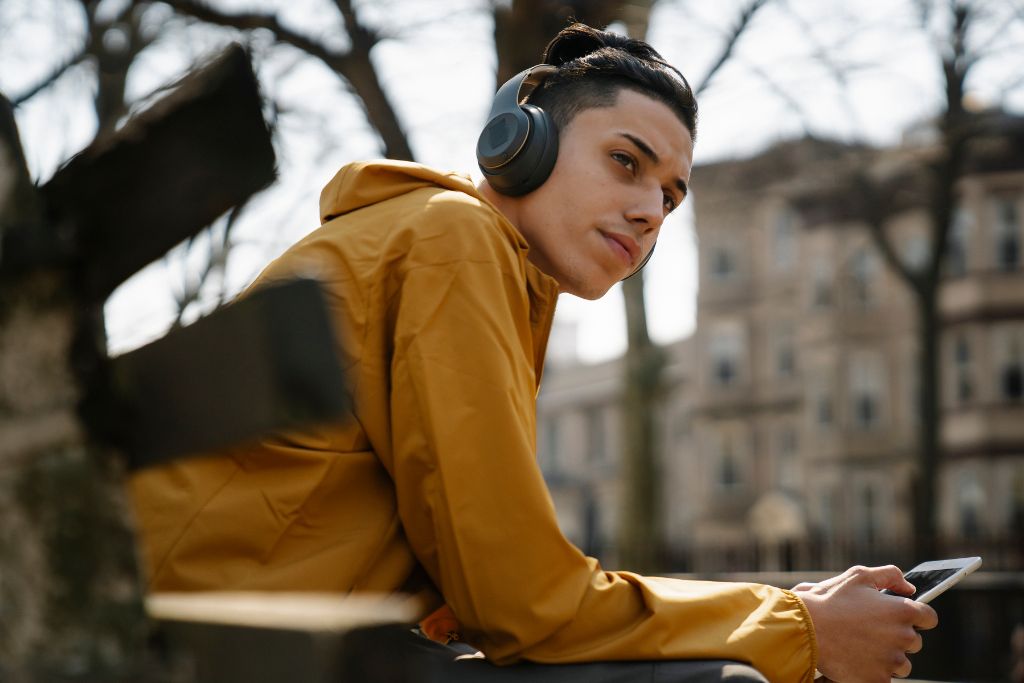 Teenage boy sitting outdoors with headphones, looking thoughtful while holding a phone