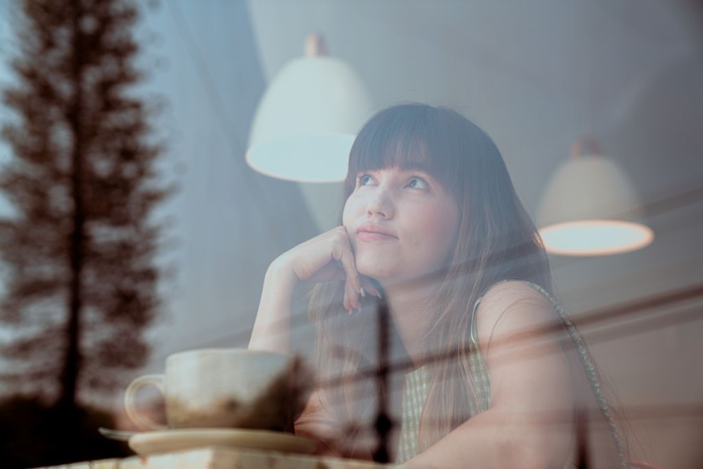 Teenage girl sitting by a window, reflecting quietly with a cup in front of her