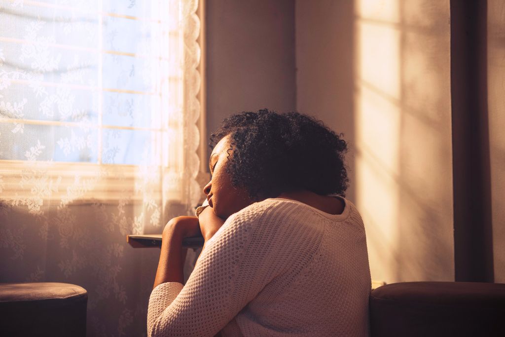 Woman sitting quietly by a window, appearing reflective and withdrawn, symbolising symptoms of trauma and emotional overwhelm