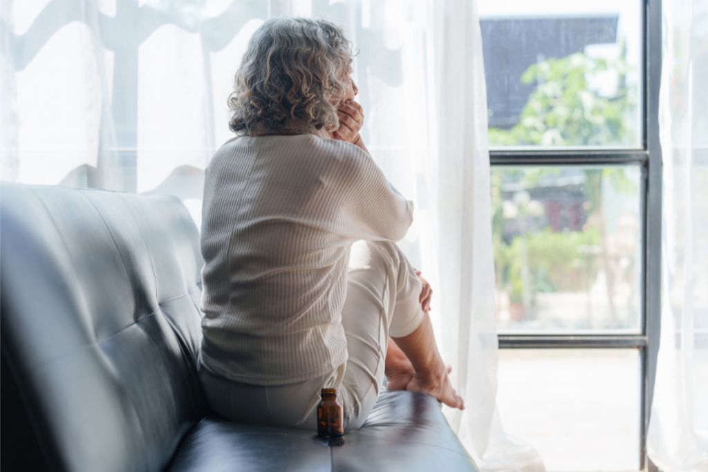 Woman sitting on a sofa looking out a window, appearing reflective and calm