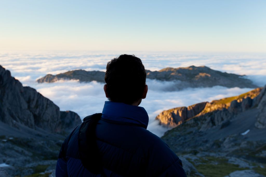 Person looking out over mountain landscape above the clouds, symbolising clarity and new perspective