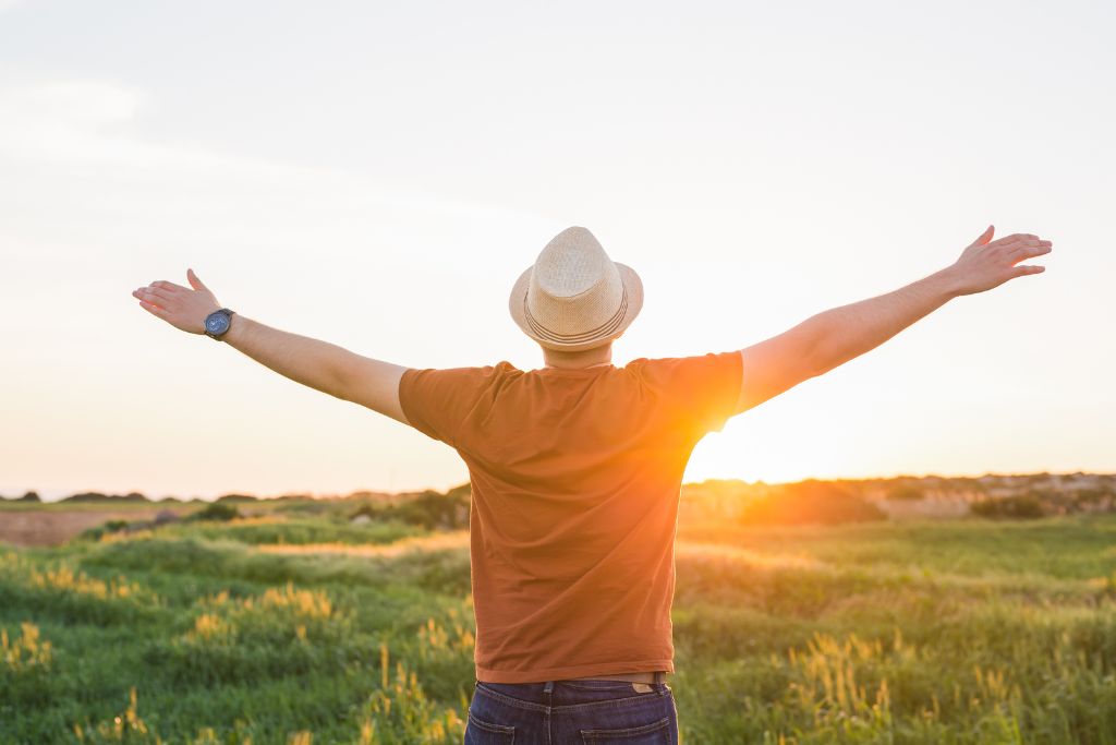 Person standing in a field at sunrise with arms open, symbolising hope and positive change