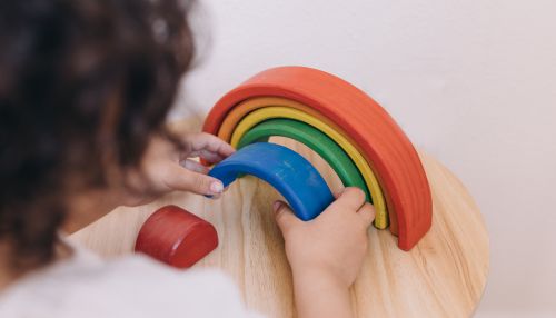 Young child engaging with a colourful wooden rainbow stacking toy during a play-based learning activity