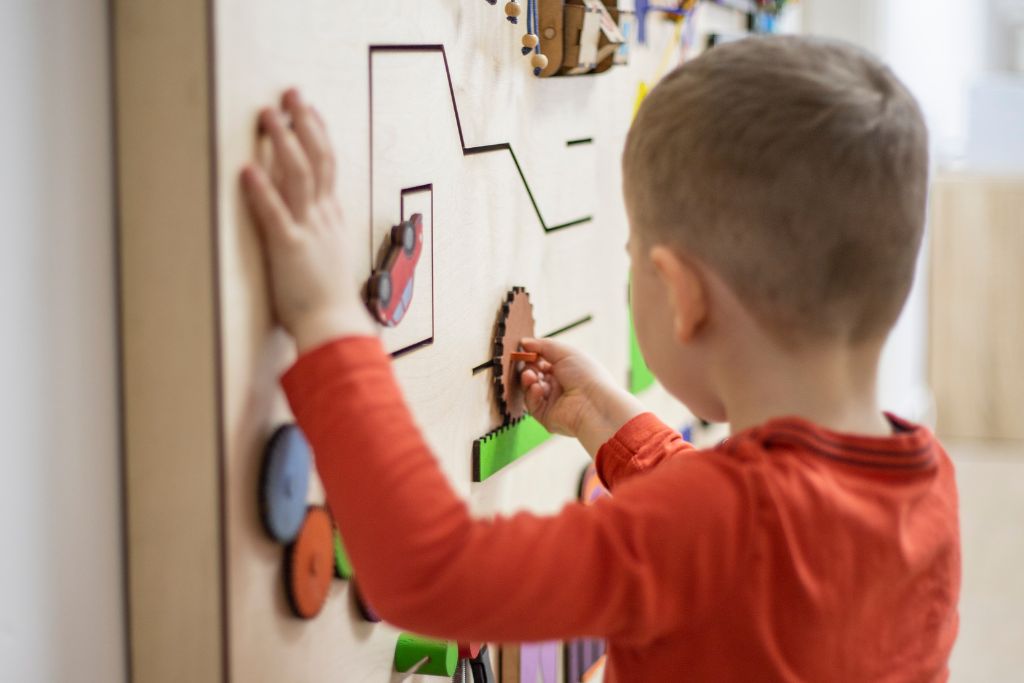 Child exploring a wall-based activity board designed for sensory and motor development