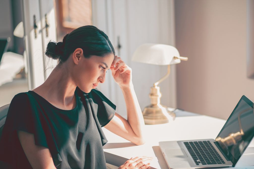 Woman looking thoughtful while seated at a laptop, reflecting mental focus and internal struggle