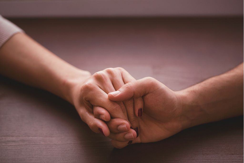 Close-up of two hands holding on a dark surface, representing reassurance and fear
