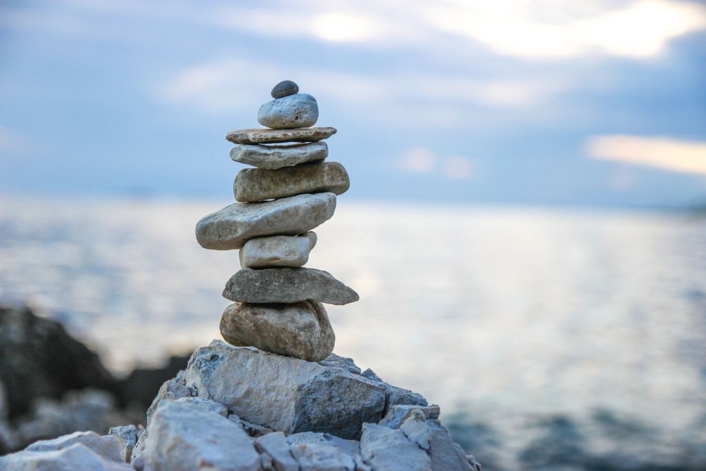 A balanced stack of stones on a rocky shore with calm water in the background, symbolising stability and mindfulness