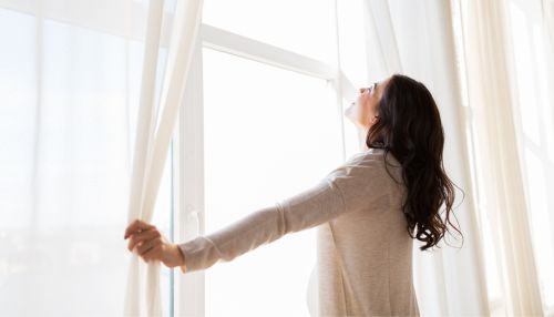Woman opening white curtains and looking up into natural light, representing openness and emotional clarity