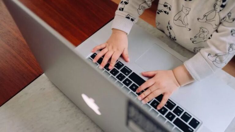Close-up of a child’s hands typing on a laptop keyboard