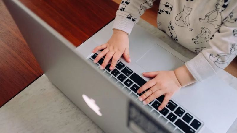 Close-up of a child’s hands typing on a laptop keyboard