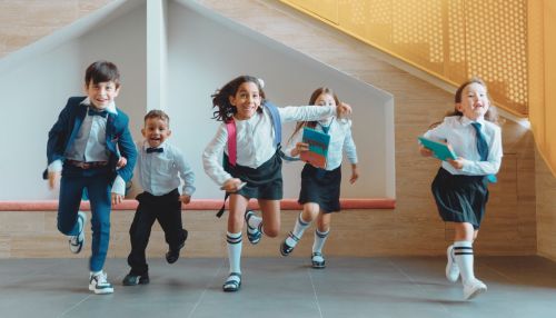 Group of primary school children running indoors in uniform, smiling and holding books – representing energy, learning and wellbeing in schools.